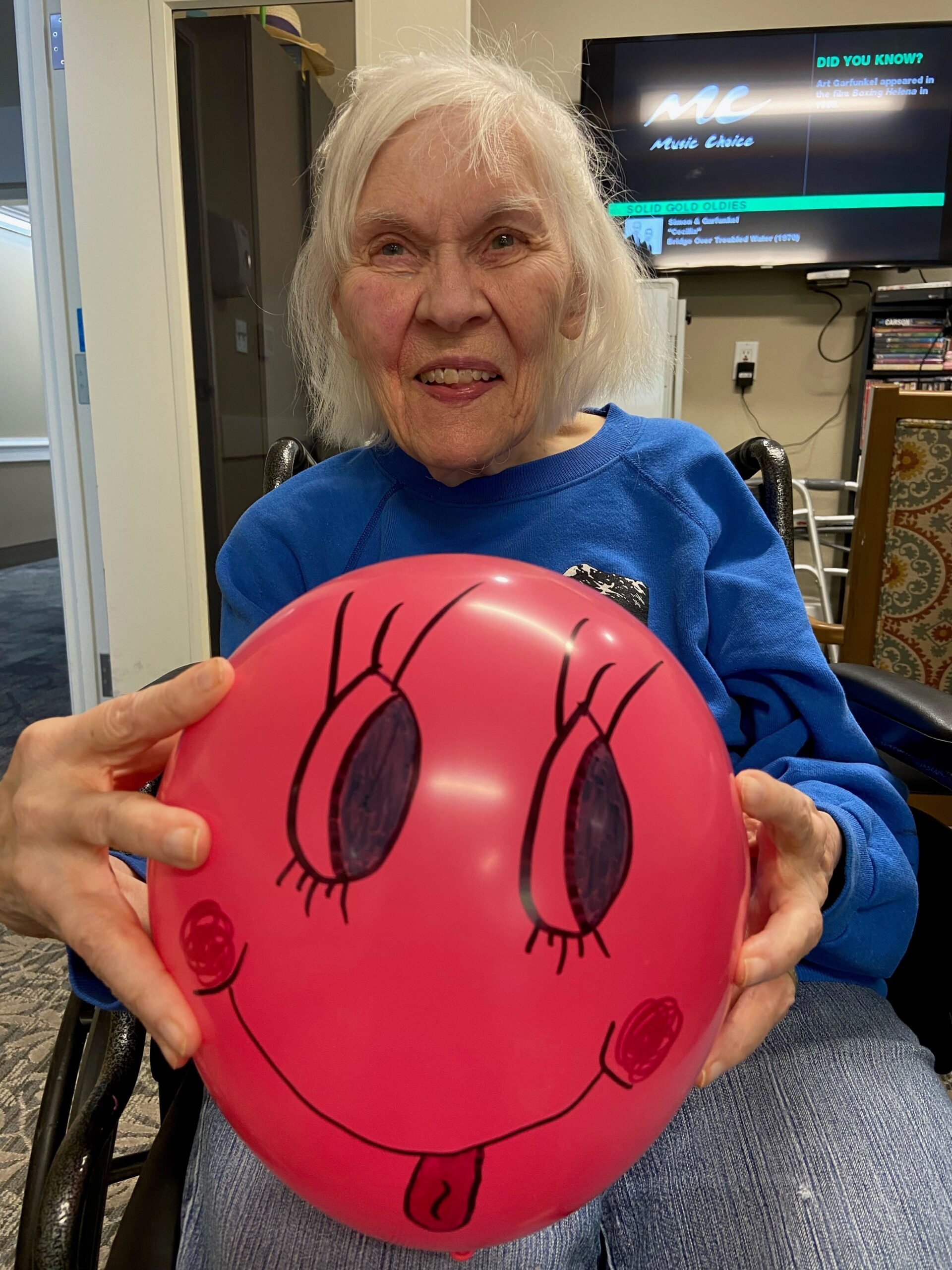 Elderly woman smiling holding smiley face balloon