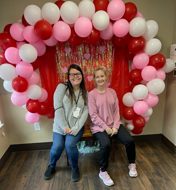 two women smiling under a balloon arch one of which is on our team of staff